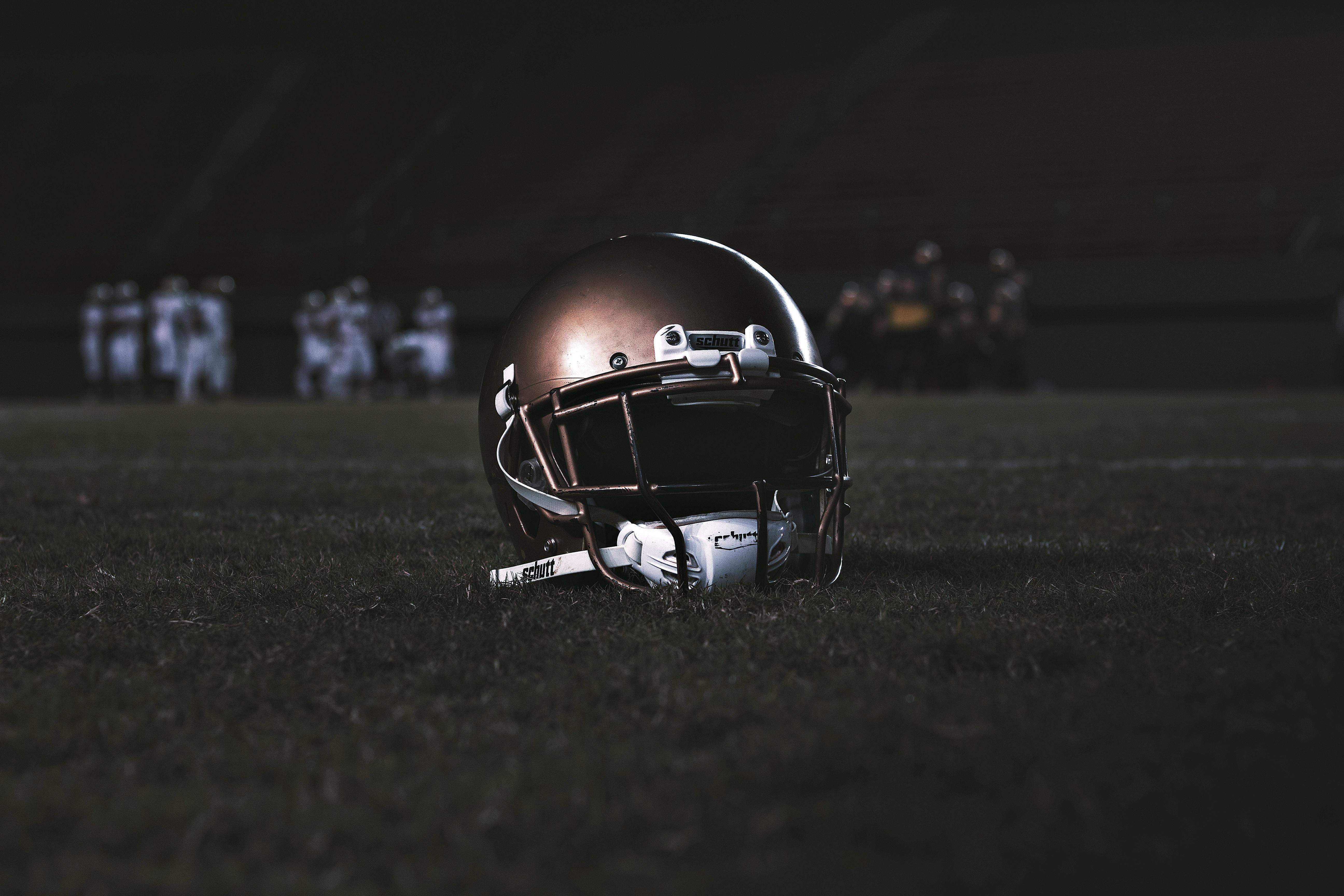 A football helmet on a dark field with a team gathered in the background.