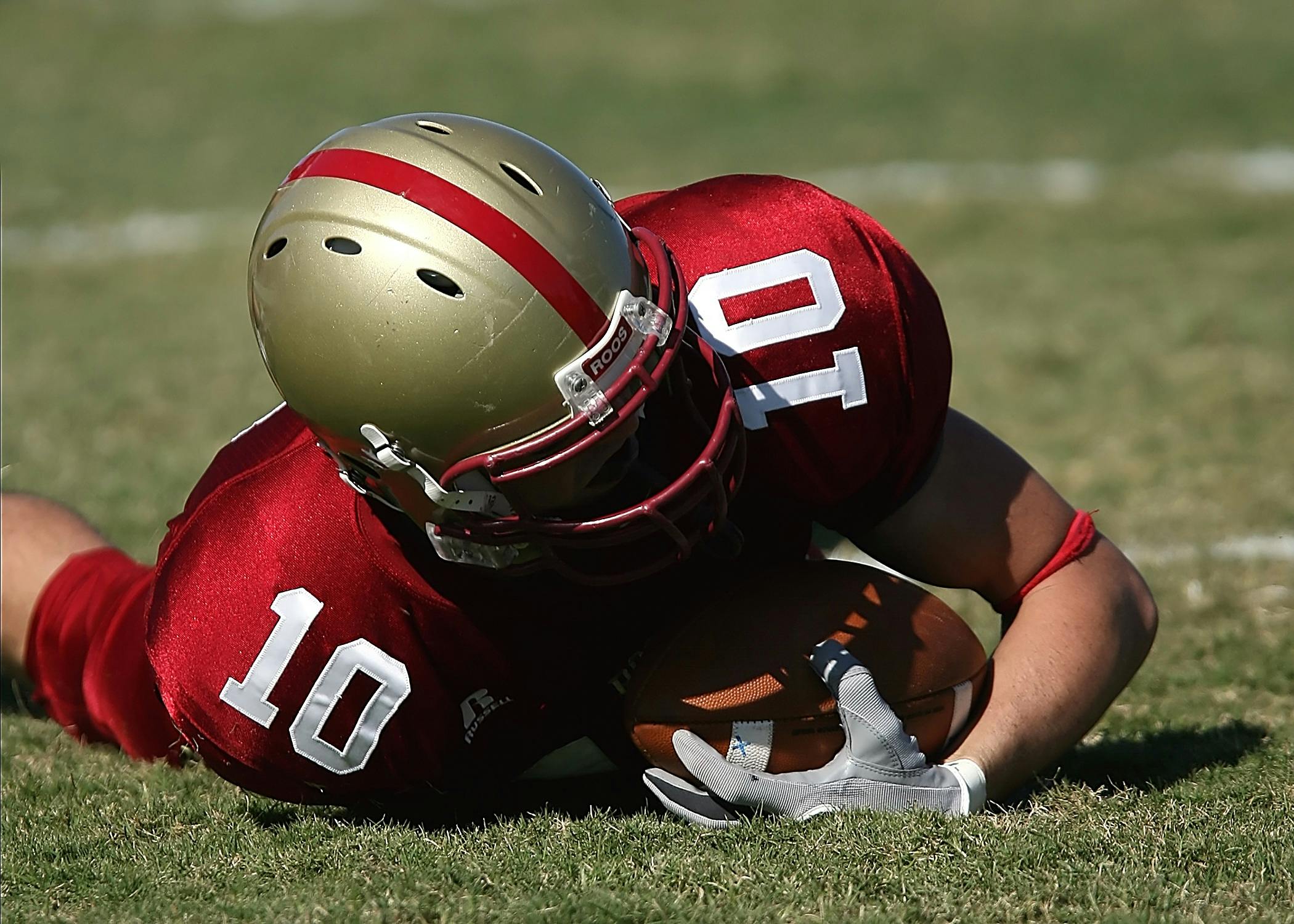 Two football teammates in red uniforms completing a tackle.